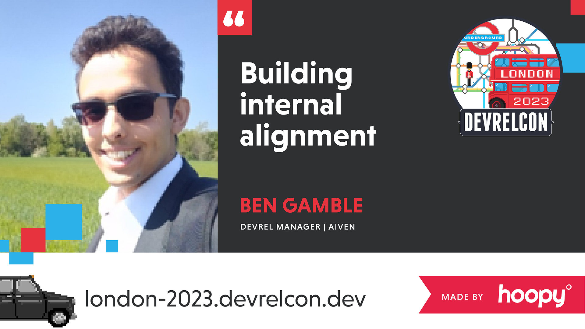 The image is a promotional banner for a speaker at a conference. It features a smiling man wearing sunglasses named Ben Gamble, who is listed as a DevRel Manager at Aiven. He will be presenting on "Building internal alignment" at DEVRELCON in London, 2023. The graphic includes iconic London imagery such as the Underground sign and a red double-decker bus. There is also a black taxi graphic at the bottom, and the event's website address, london-2023.devrelcon.dev, is included. The banner indicates that it was made by Hoopy.
