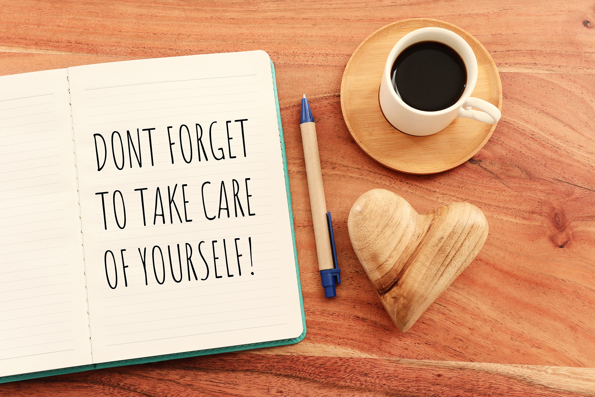 Cup of coffee next to a notebook that reads, "Don't forget to take care of yourself"